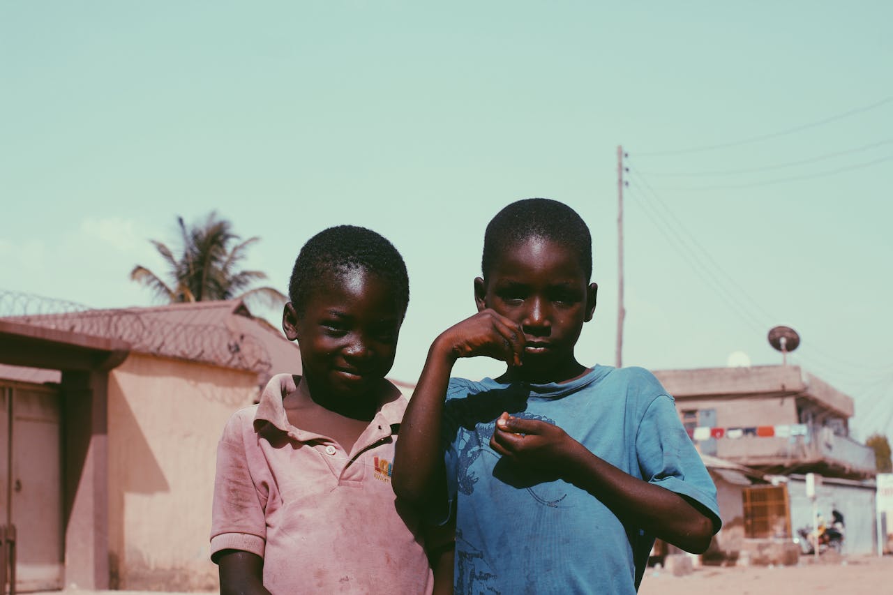Two African boys smiling and posing outdoors, showcasing friendship in a rural setting.