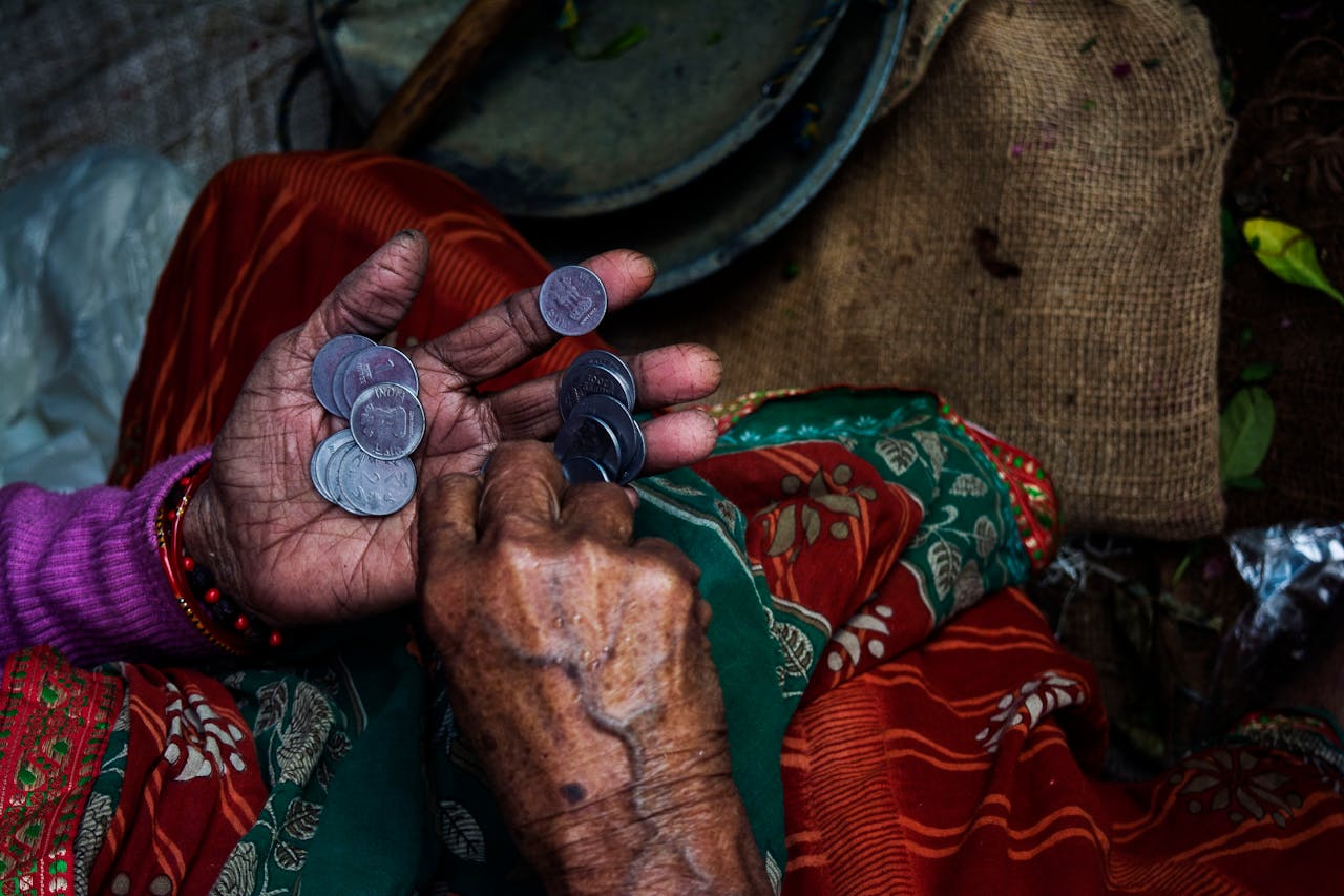 Close-up of an elderly woman's hands counting coins on a colorful textile background.